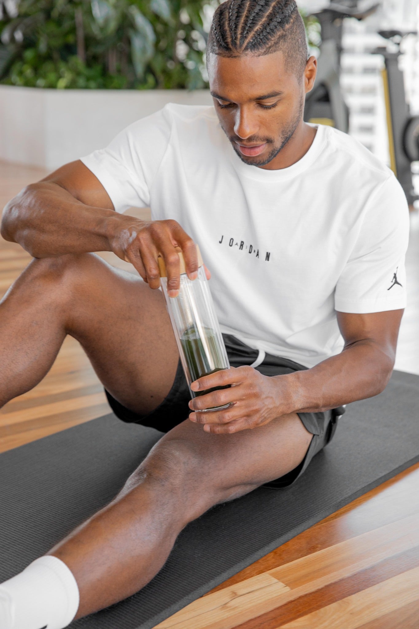 Man sitting on a gym mat and preparing a drink with Alk Labs A.M Greens powder, highlighting the supplement's convenience for fitness enthusiasts. This organic, non-GMO, vegan-friendly powder supports optimal health, boosts energy, and enhances natural detoxification.