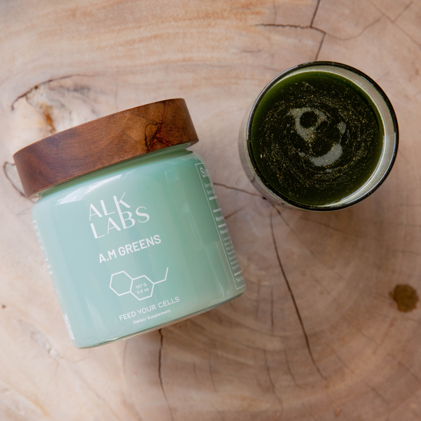 Alk Labs A.M Greens powder, a premium organic, non-GMO supplement designed to support optimal health, gut health, and boost immunity. Shown on a natural wooden surface with a serving of mixed greens powder, highlighting its natural ingredients and health benefits. Ideal for daily use to promote overall wellness and energy.